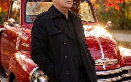 بورتريه سينمائي فائق الواقعية لرجل متكئًا على الصدام الأمامي لشاحنة شيفروليه بيك-أب كلاسيكية لامعة باللون الأحمر من خمسينيات القرن الماضي