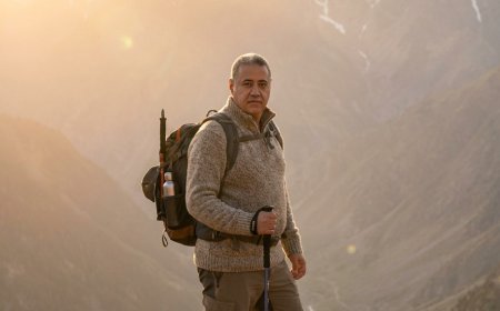 يصوّر المشهد منظرًا جبليًا شاسعًا خلال الساعة الذهبية، حيث تلقي الشمس ضوءًا دافئًا على القمم المغطاة بالثلوج